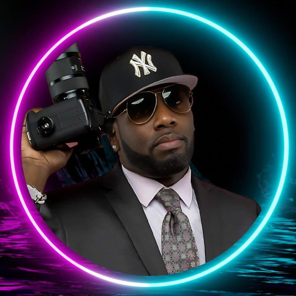 Micah Berkley in a dark suit and NY cap, holding a camera, with a neon light circle framing him against a dark backdrop.